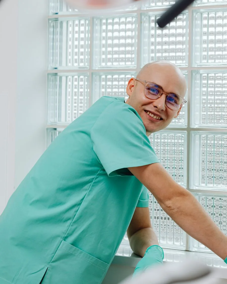 Photograph of a dentist in green scrubs beside a treatment light in a clinic