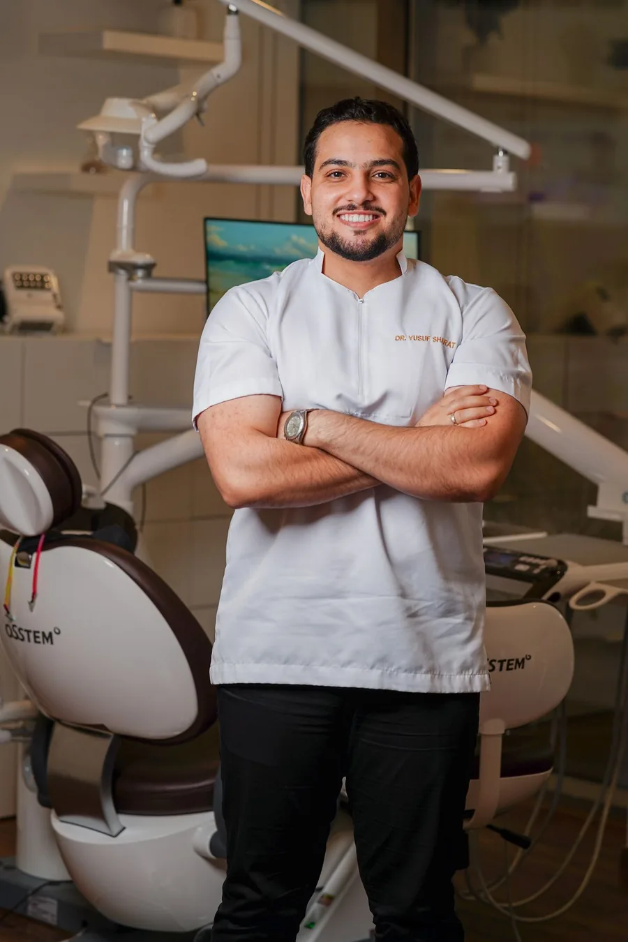 Photograph of a dentist in a white tunic standing beside a dental treatment chair