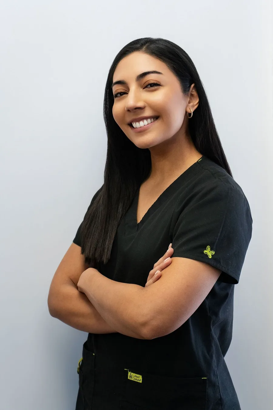 Photograph of a dentist in dark scrubs with arms folded